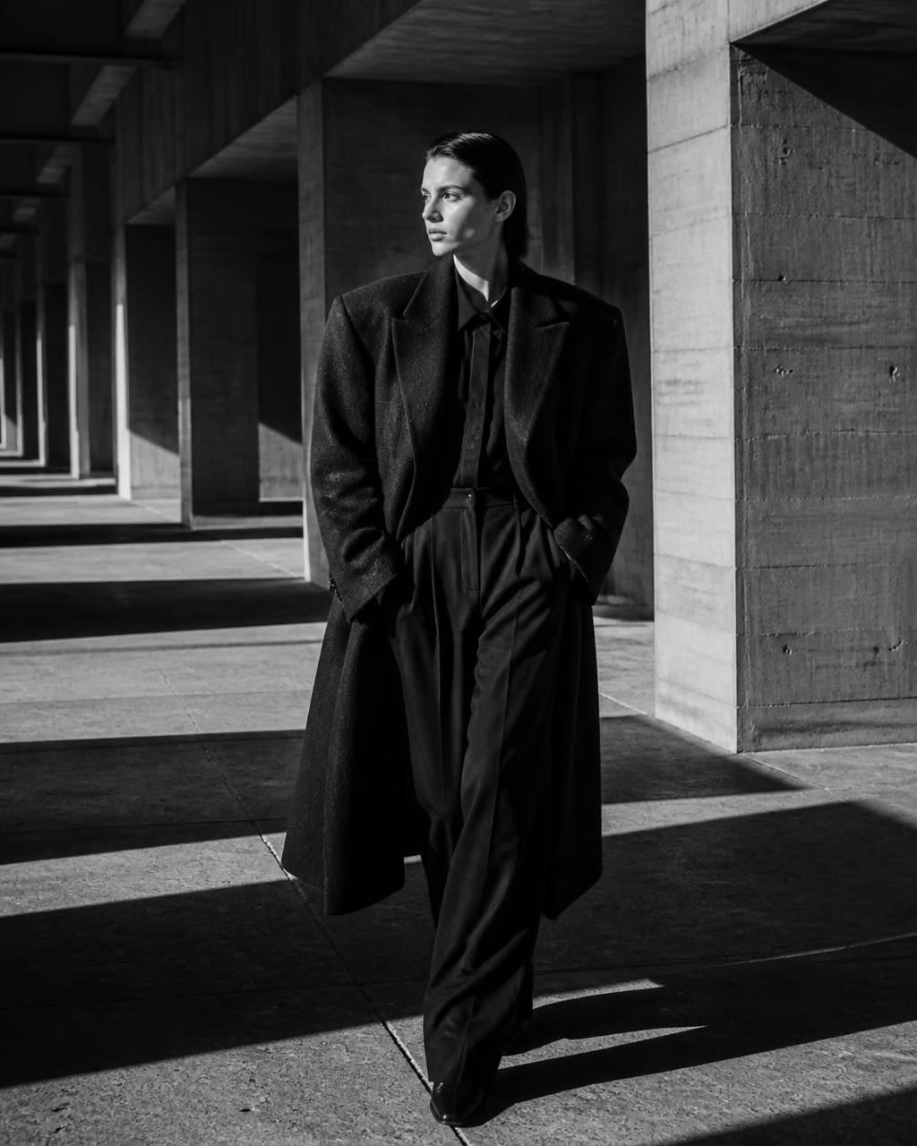 High fashion campaign photograph of a model in a tailored coat against concrete architecture